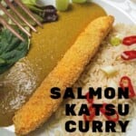 A white plate with a breaded salmon fillet, katsu curry sauce, rice and salad. Garnished with chillis.