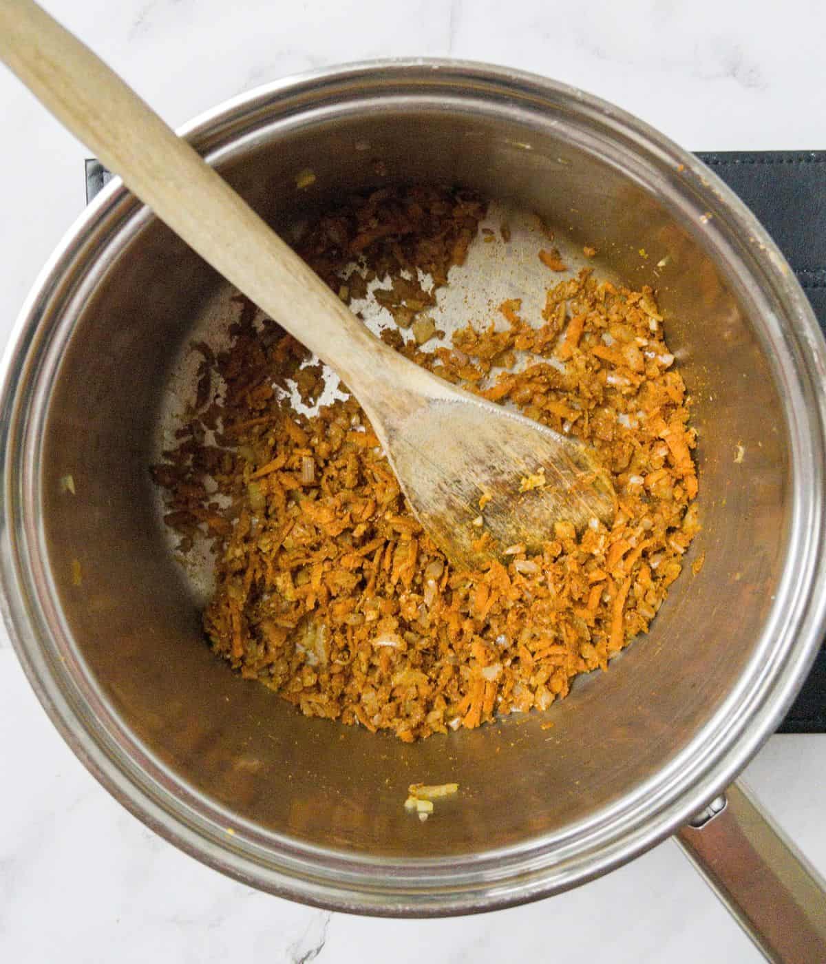 chopped onion, carrots and spices being stirred in a saucepan.