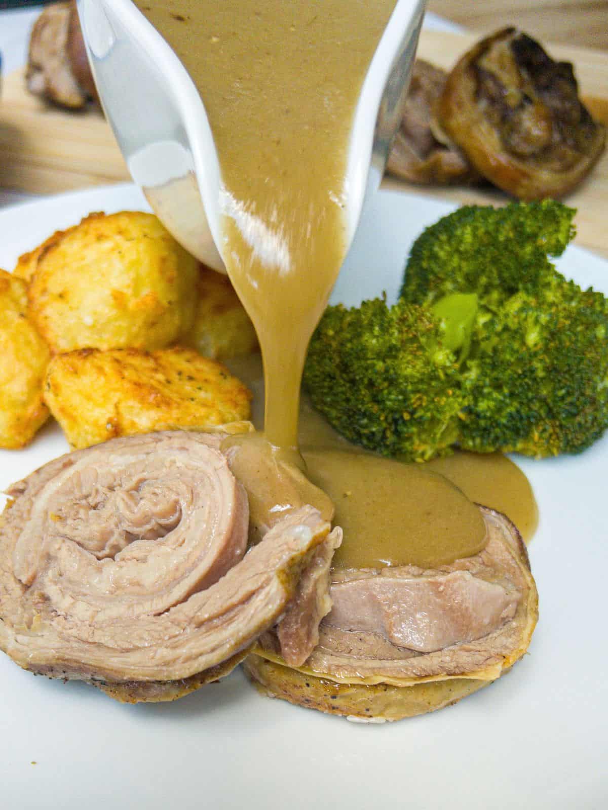 Gravy being poured onto a plate containing lamb breast, roast potatoes and broccoli.