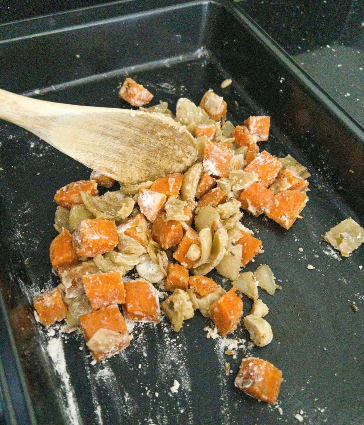 Onions and carrots in a pan with flour being stirred.
