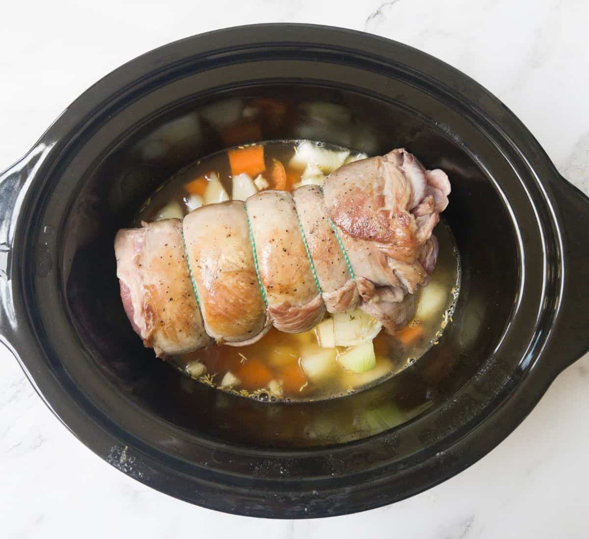 lamb breast laying on a bed of veg and stock in a slow cooker.