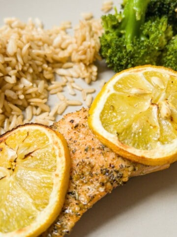 Trout fillet garnished with lemon on a plate with rice and broccoli.
