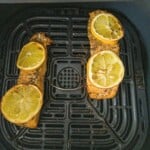 Two cooked trout fillets garnished with lemon in the air fryer.