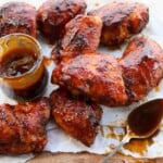 BBQ chicken thighs with a pot of BBQ sauce and a spoon covered in BBQ sauce.