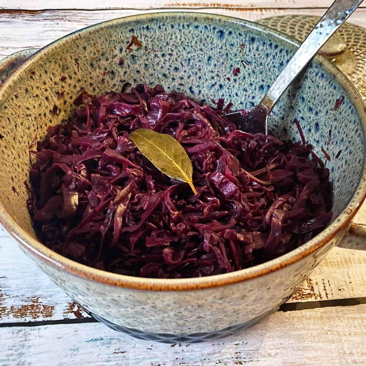 Braised red cabbage in a casserole dish with a spoon. Garnished with a bayleaf.