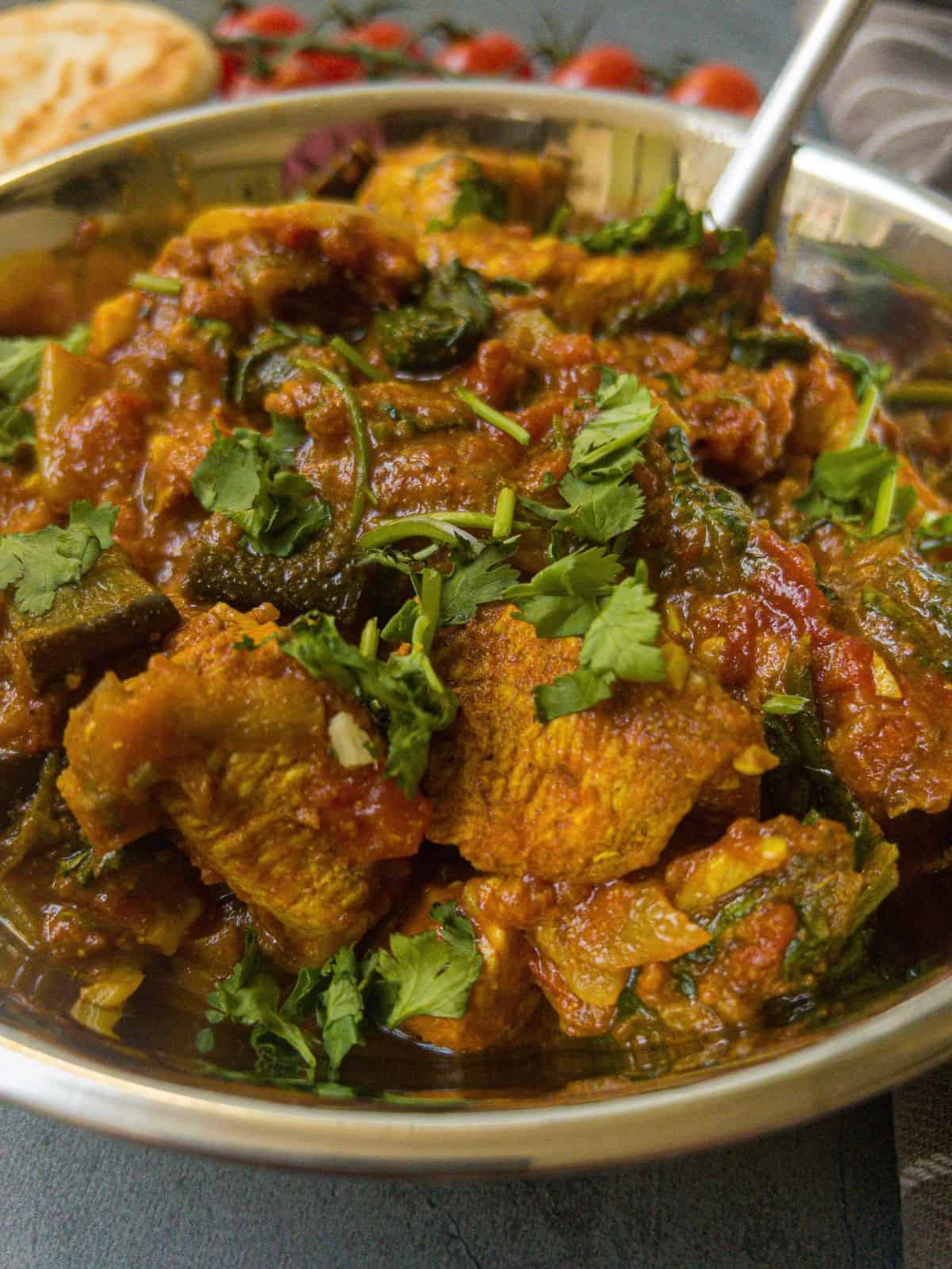 Chicken and aubergine curry in a silver balti dish garnished with coriander.
