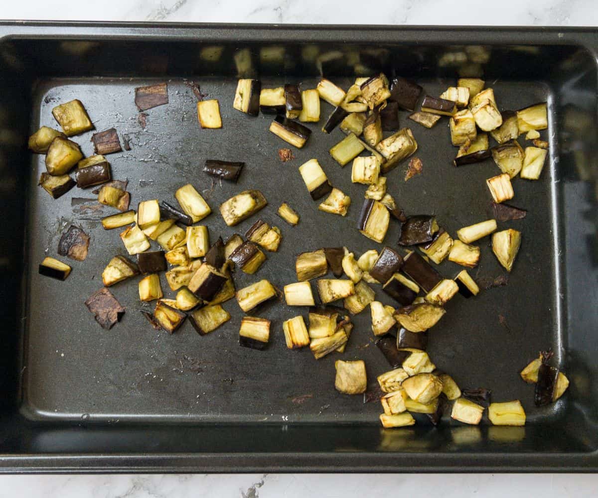 Chunks of roasted aubergine on a baking tray.