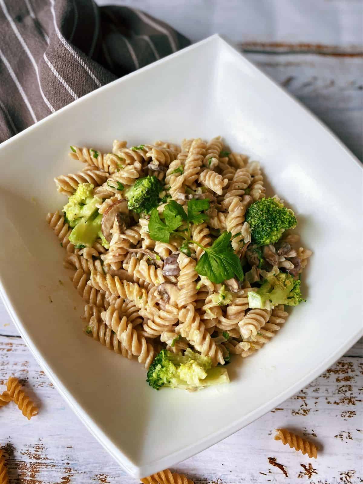 Fusilli pasta with broccoli and mushroom in a white square bowl, garnished with parsley.