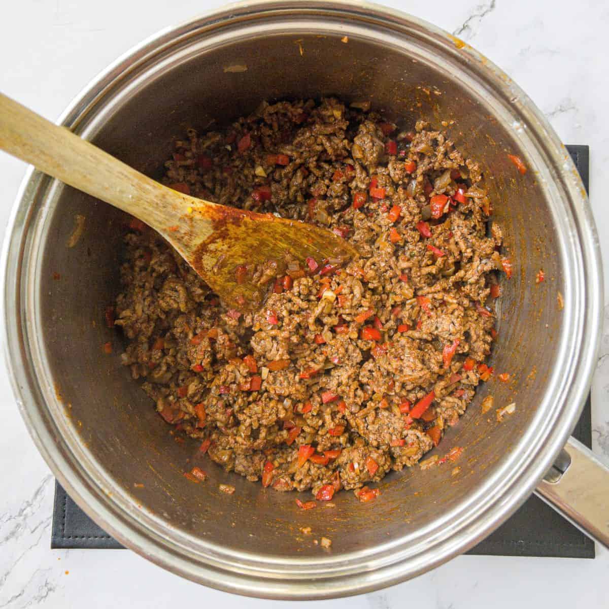Minced beef and chilli being cooked in a saucepan. A wooden spoon is in the saucepan.