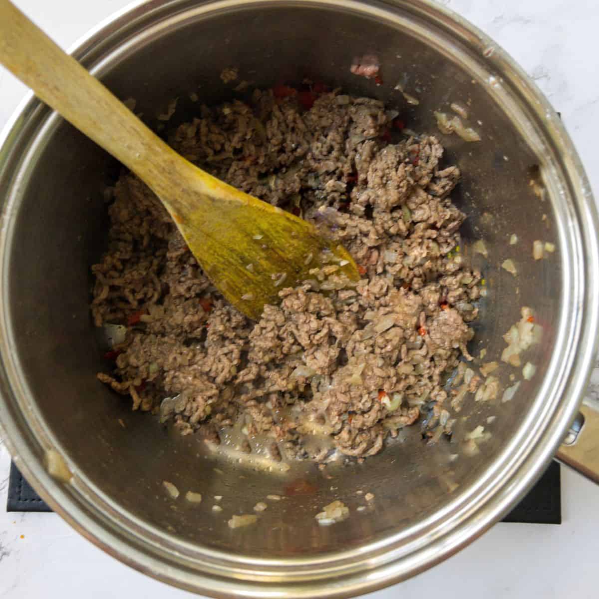 Mince beed being fried in a saucepan, being stirred with a wooden spoon.