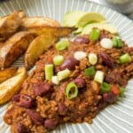 Chilli con carne on a plate with some potato wedges. Garnished with spring onion.
