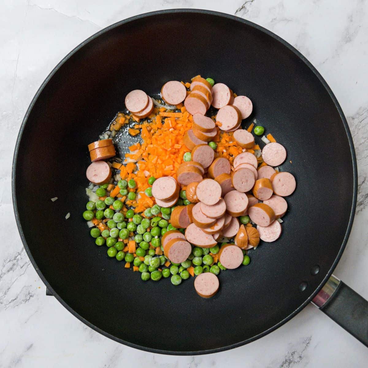 Hot dog slices, peas and carrots in a wok.