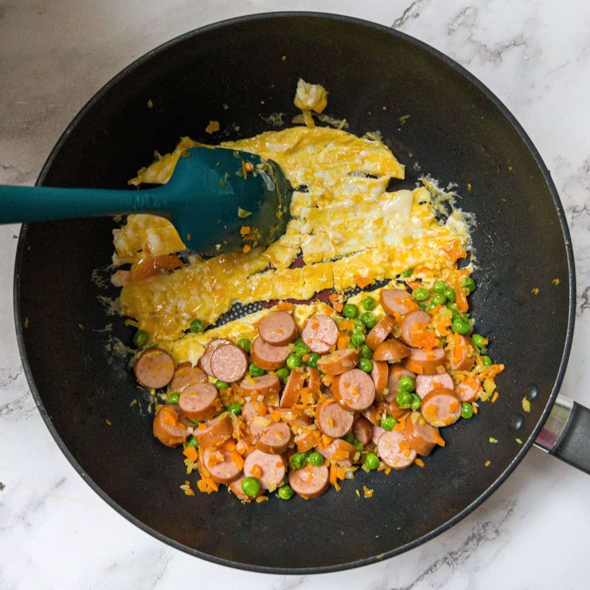 Hot dog fried rice in a wok with an omelette of egg being sliced with a spatula.