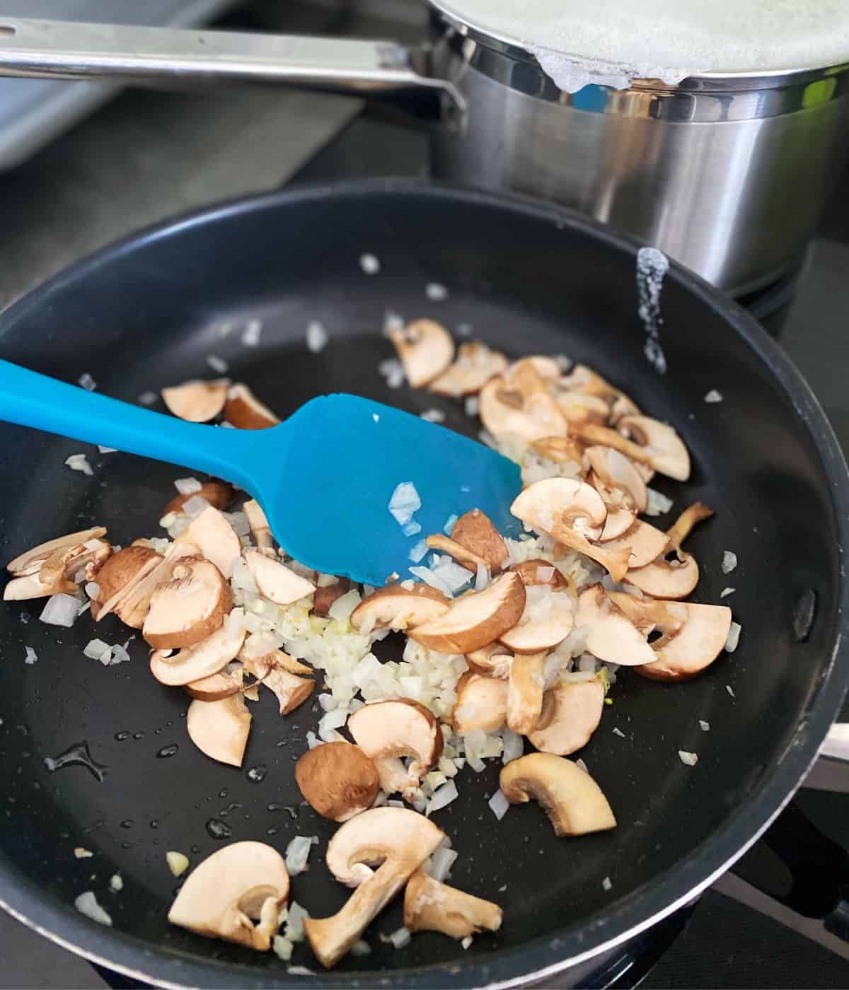 Mushrooms, onion and garlic being stirred in a frying pan.