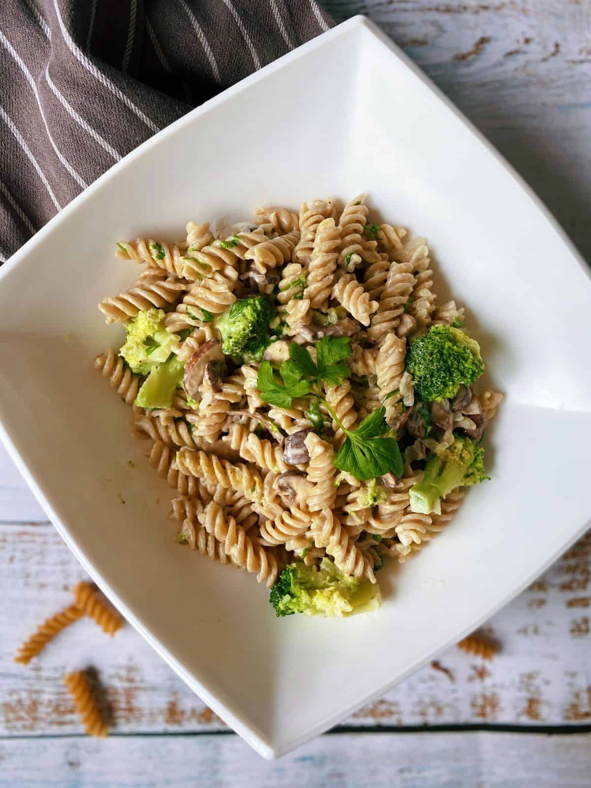 Fusilli pasta with broccoli and mushroom in a white square bowl, garnished with parsley.