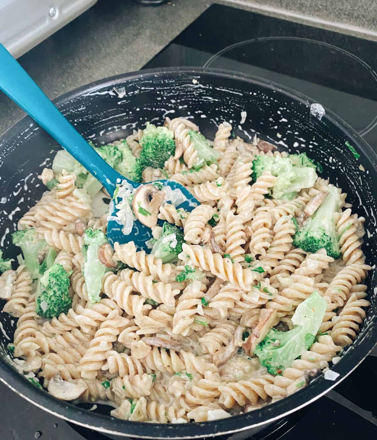 Creamy fusilli pasta with broccoli and mushroom being stirred in a frying pan.