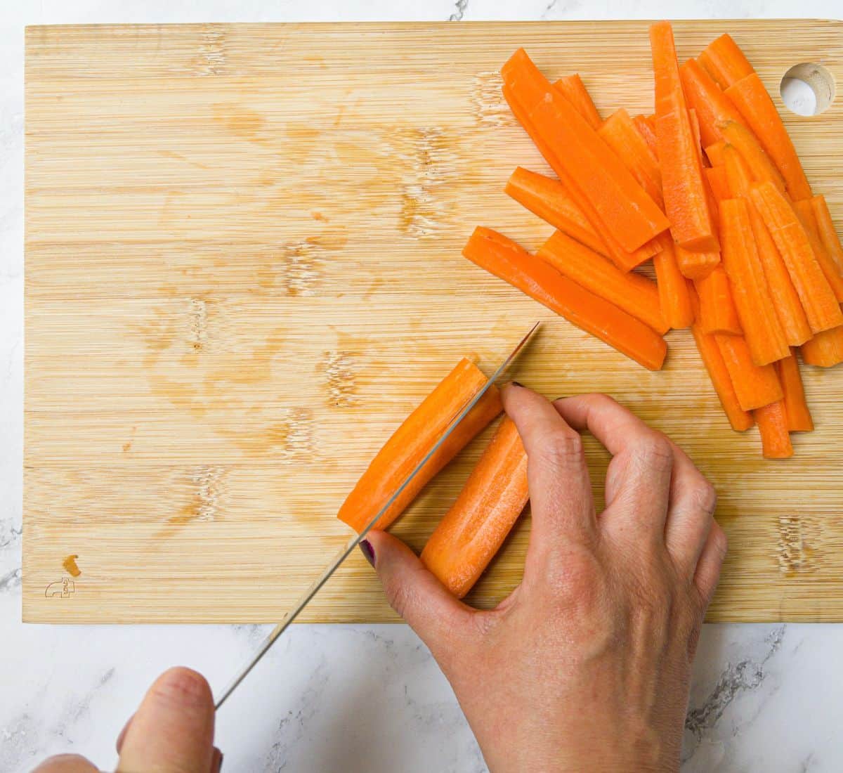 Carrots being chopped into sticks on a chopping board.