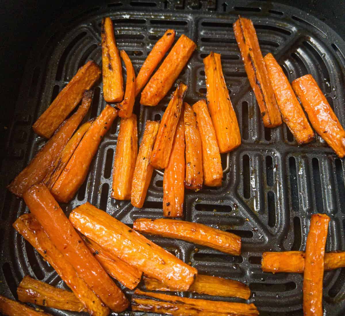 cooked carrot sticks in an air fryer basket.