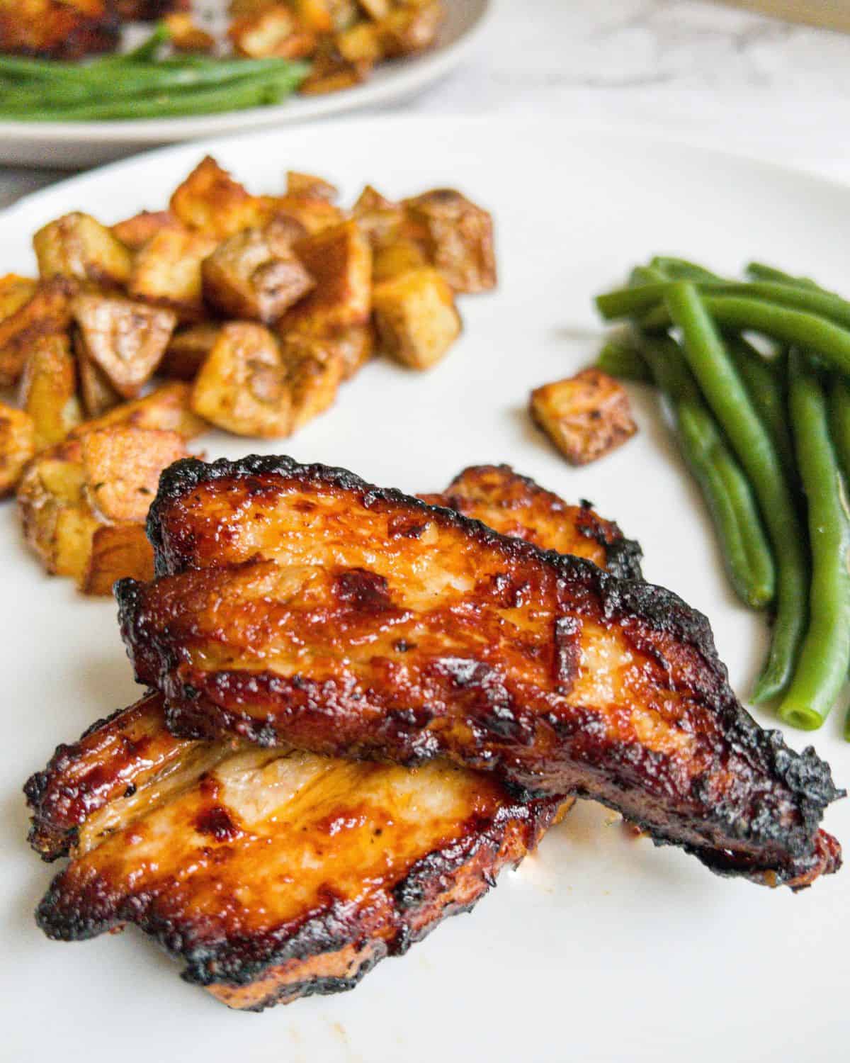 Pork belly strips, potatoes and green beans on a white plate.