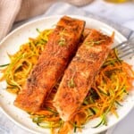 Two salmon filletson a bed of noodles on a white plate.