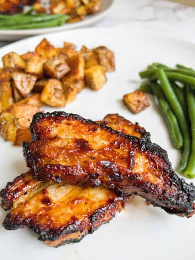 Pork belly strips, potatoes and green beans on a white plate.