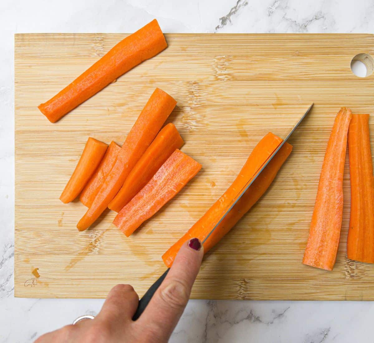 Carrots being chopped into sticks on a chopping board.