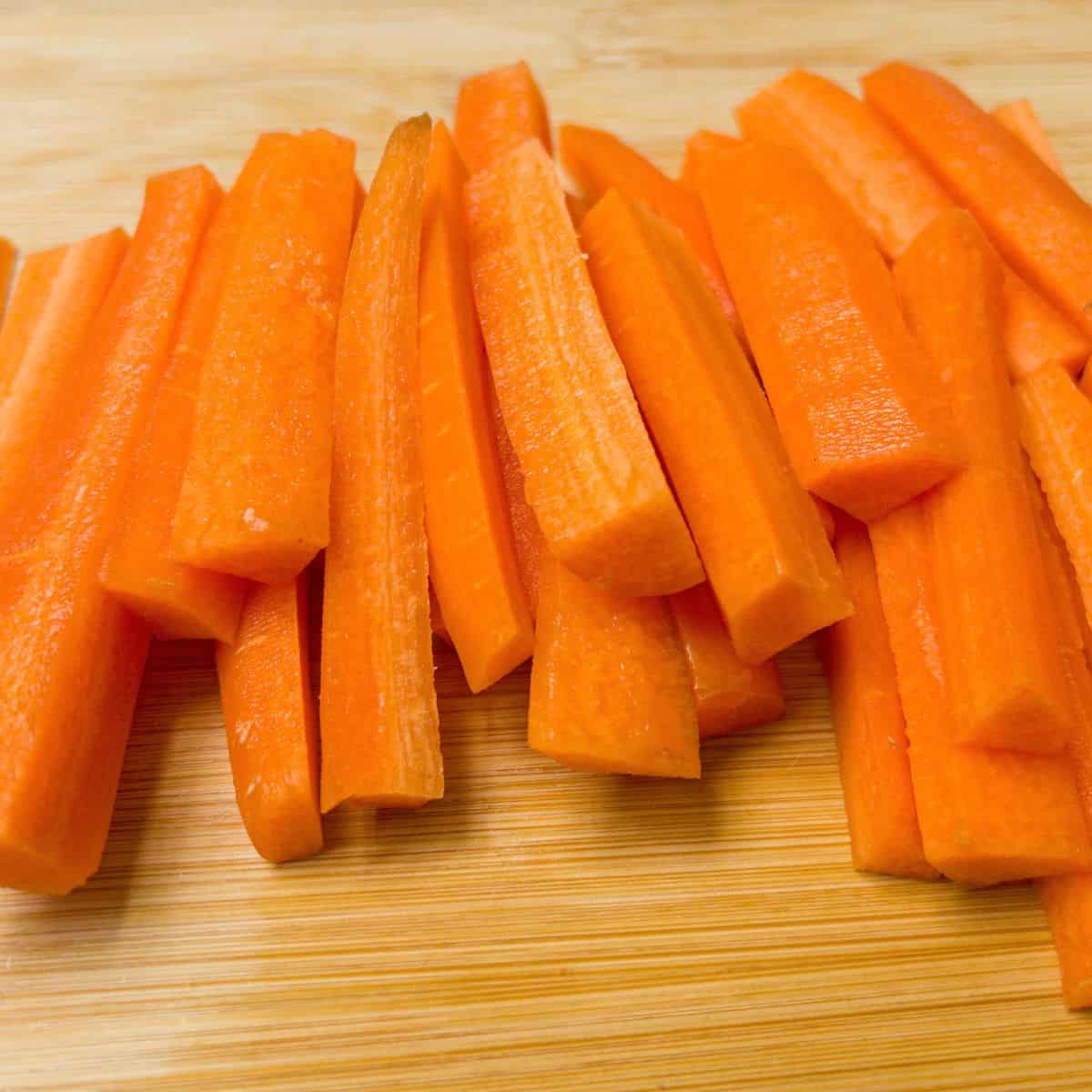 Carrots chopped into batons on a chopping board.