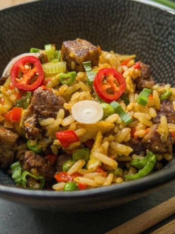 Bowl of pork belly fried rice garnished with red chilli and spring onion.