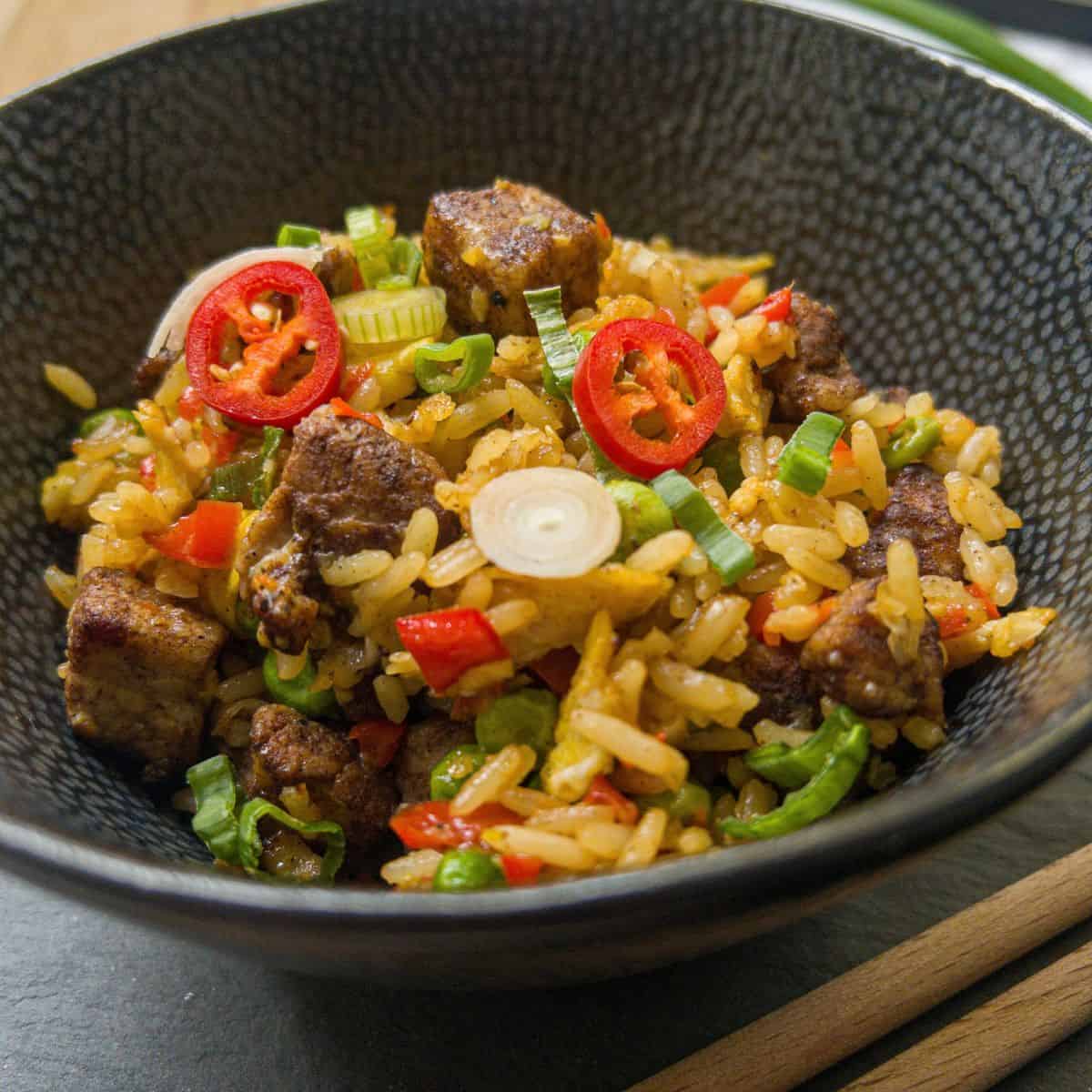 Bowl of pork belly fried rice garnished with red chilli and spring onion.