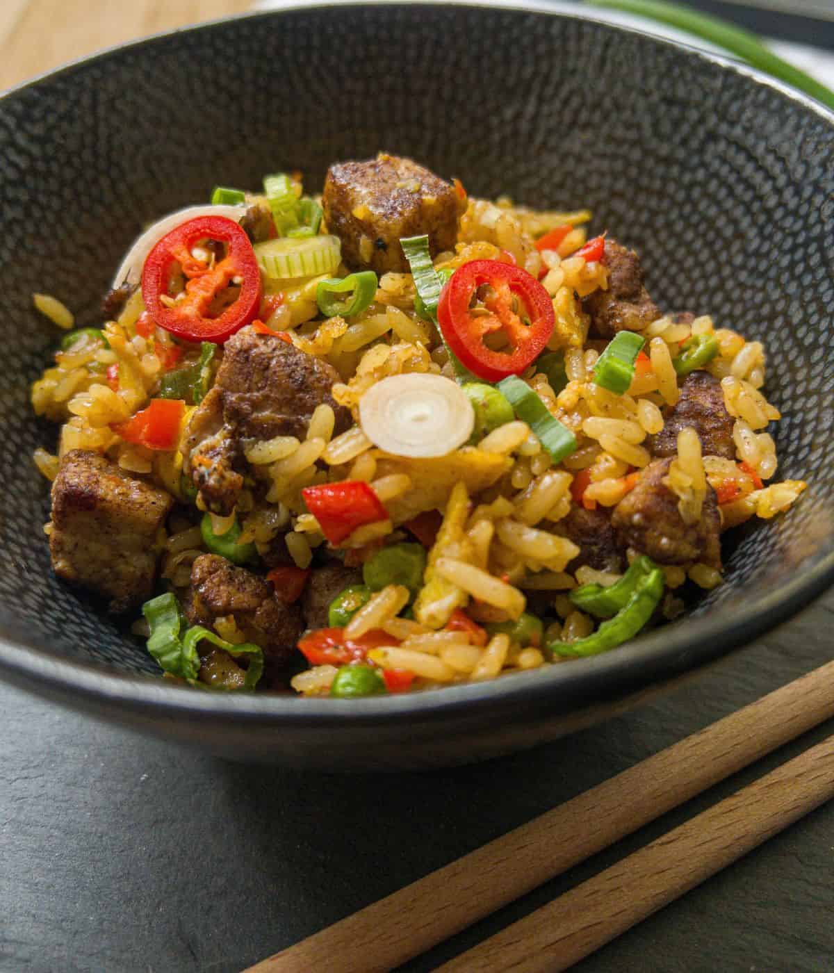 Bowl of pork belly fried rice garnished with red chilli and spring onion.