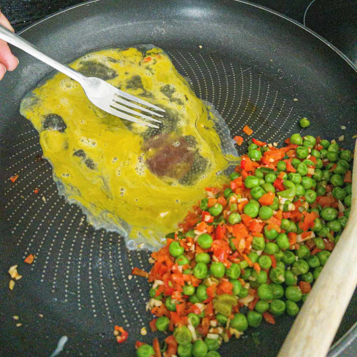 Peas and red pepper on one side of frying pan and eggs being scrambled in the other side.