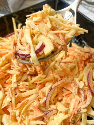 A spoonful of coleslaw over a bowl of coleslaw.