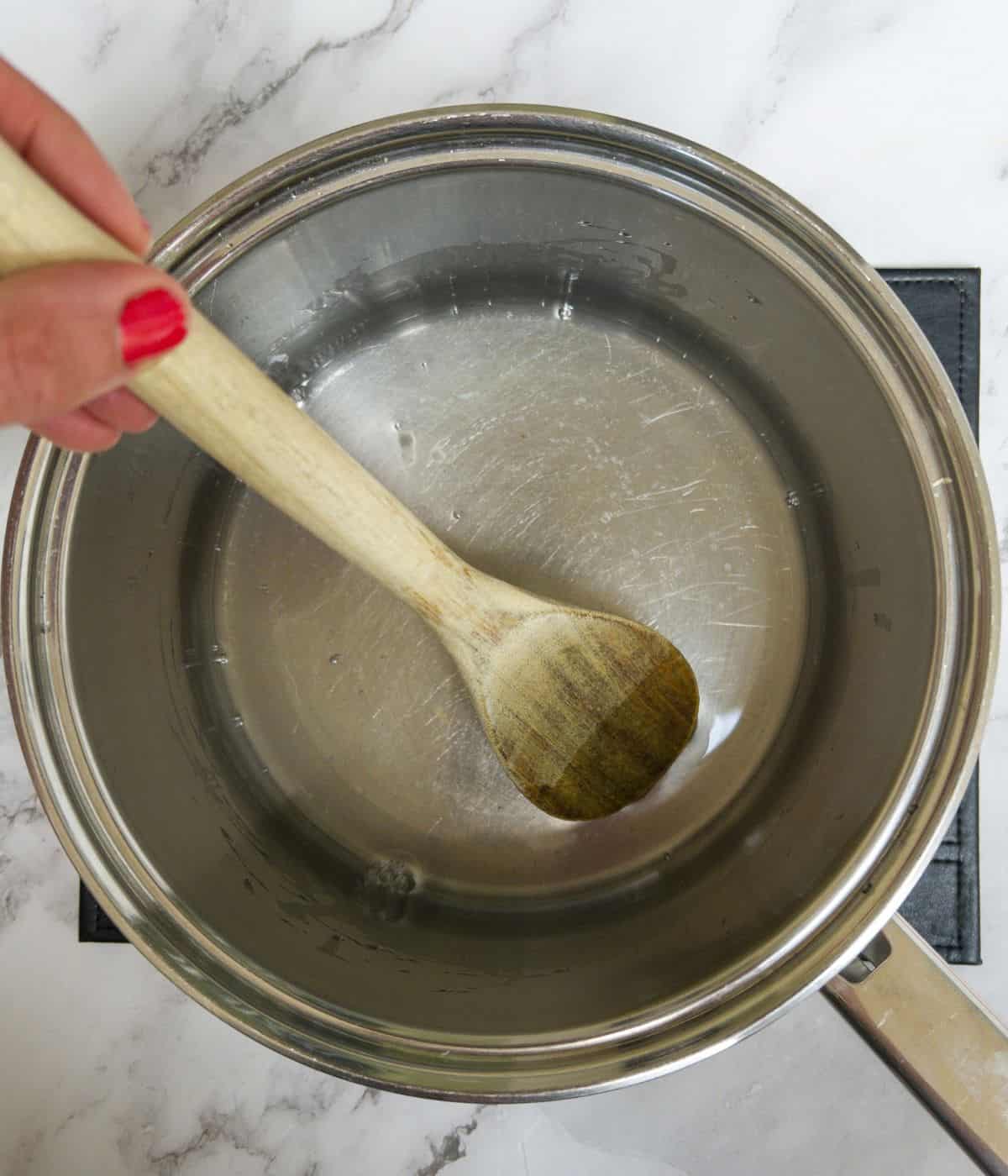 Melted coconut oil in a saucepan being mixed with a wooden spoon.
