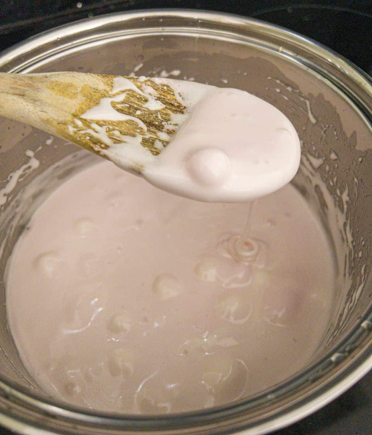 Melted marshmallows in a saucepan being mixed with a wooden spoon.