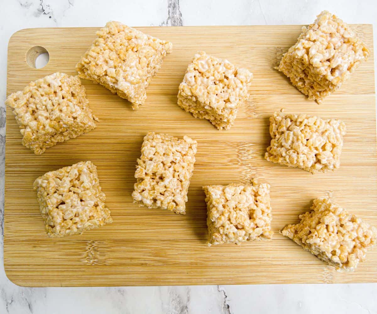 Squares of rice krisipies coated in marshmallows on a wooden chopping board.