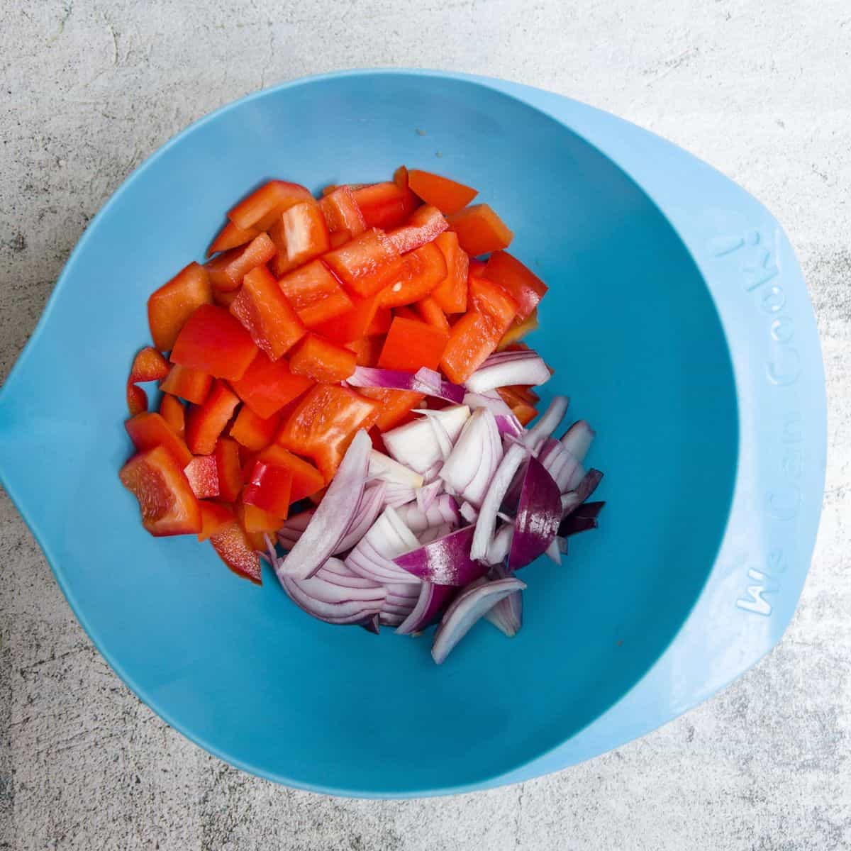 Chunks of red pepper and red onion raw in a blue bowl.