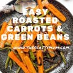 A black plate containing roasted carrots and green beans.
