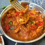 Someone taking some chicken curry out of a silver bowl with a fork.