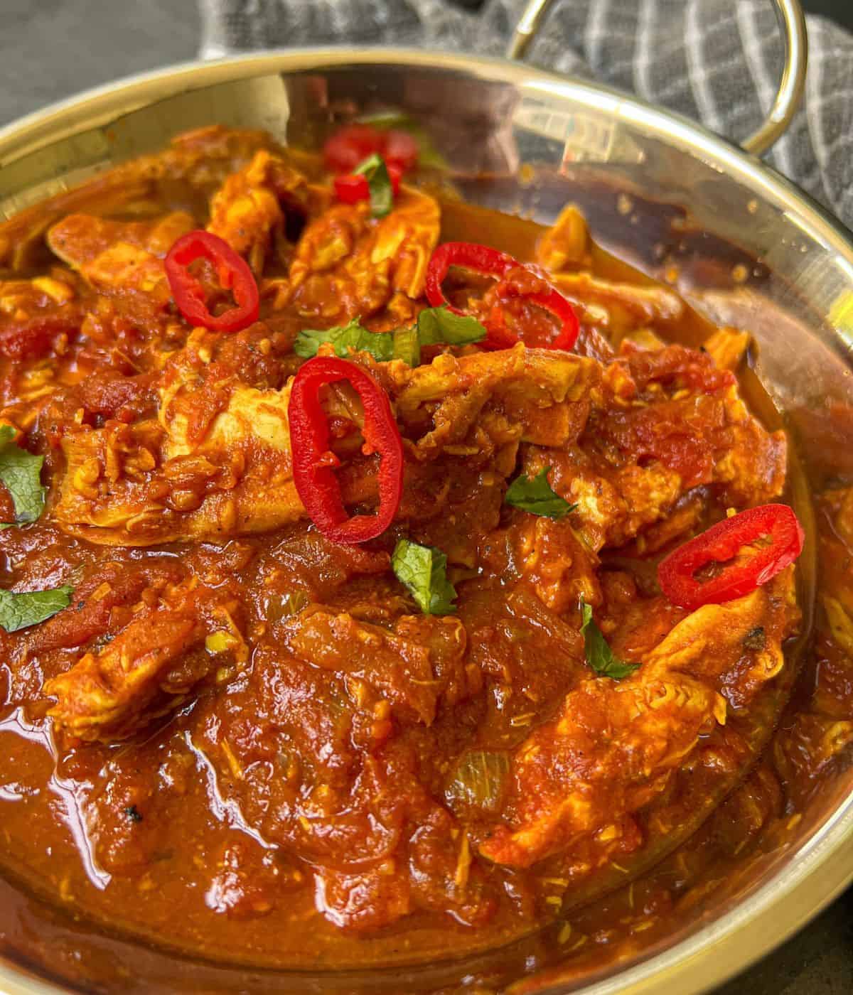 A bowl of chicken curry garnished with red chilli.