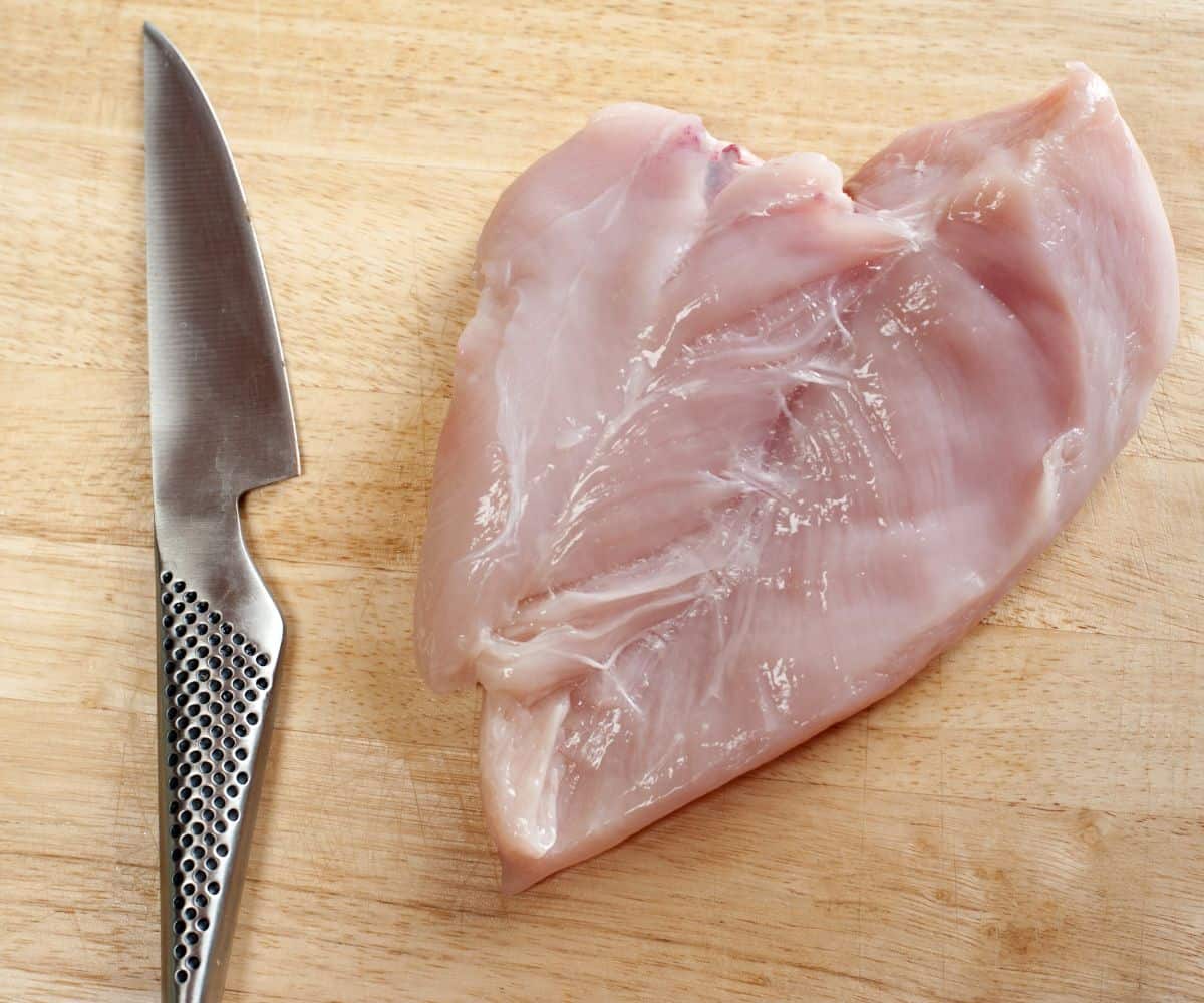 A raw butterflied chicken breast laid on a chopping board with a knife.