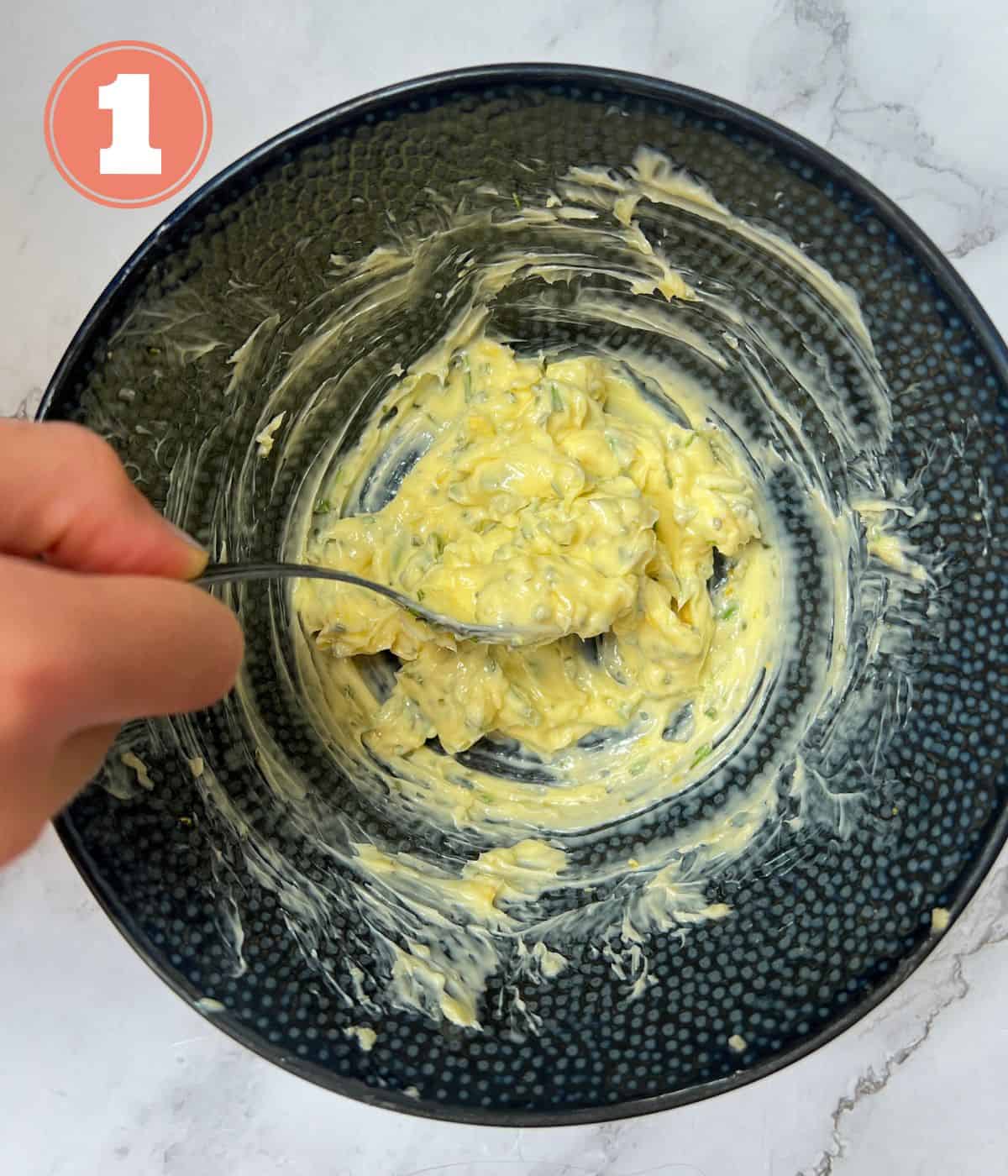 Garlic butter being stirred in a black bowl.