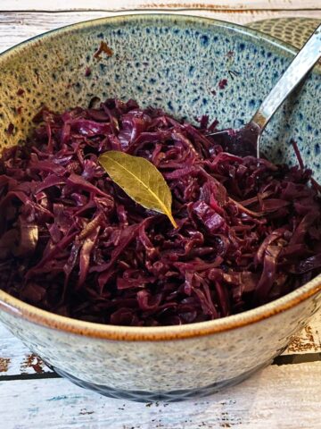 A casserole dish filled with cooked red cabbage, garnished with a bay leaf.