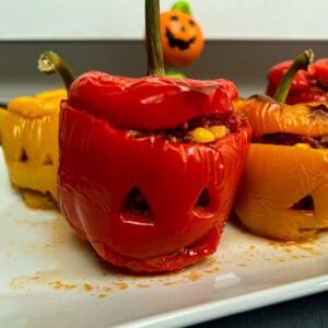 Three stuffed peppers with faces carved into them on a white plate.