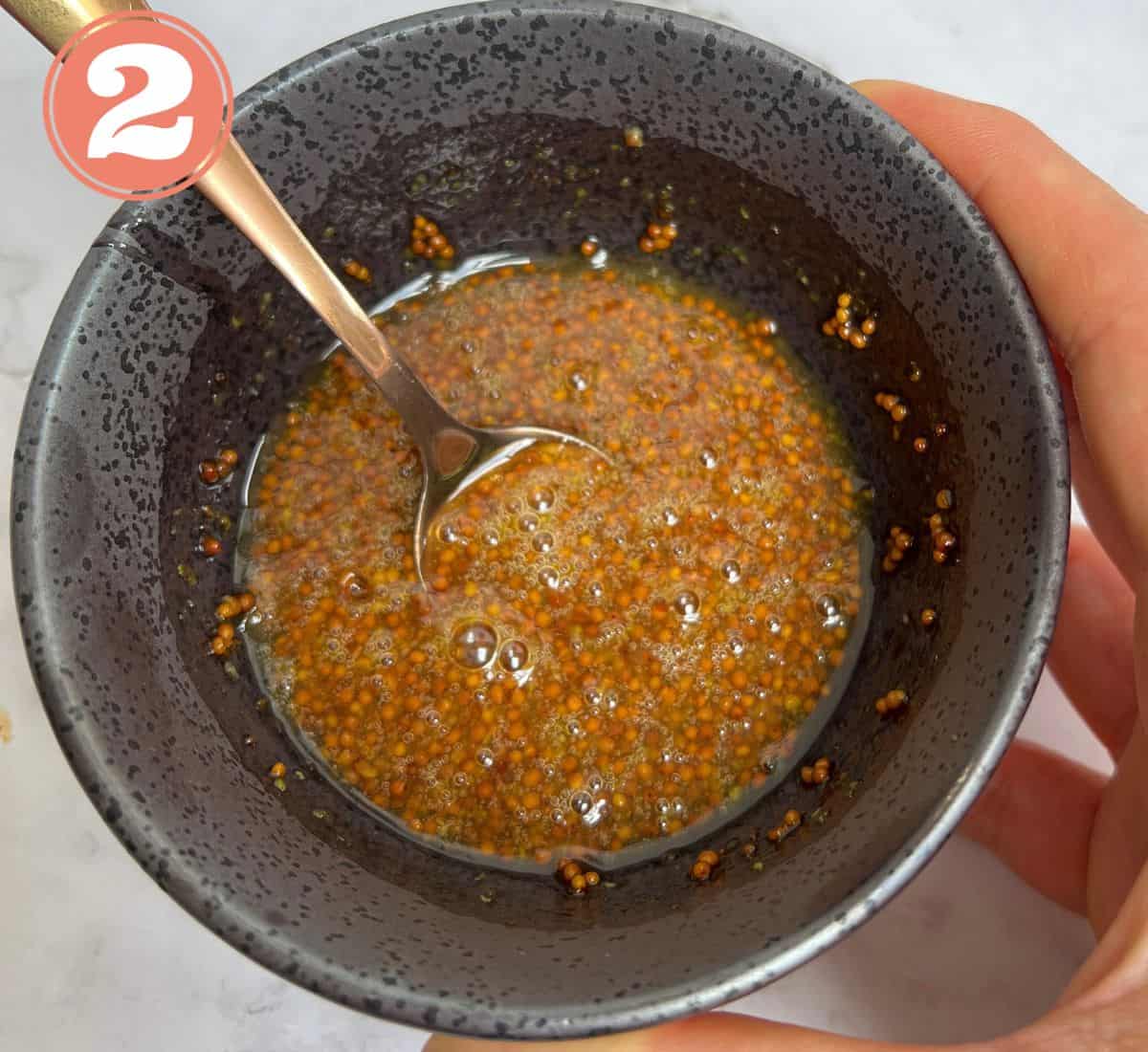 Honey and mustard marinade in a black bowl with a spoon in it.