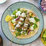 Two lamb koftas drizzled with yoghurt of a bed of salad and a flatbread on a plate with a wedge of lemon.