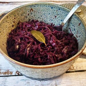 A casserole dish filled with cooked red cabbage, garnished with a bay leaf.