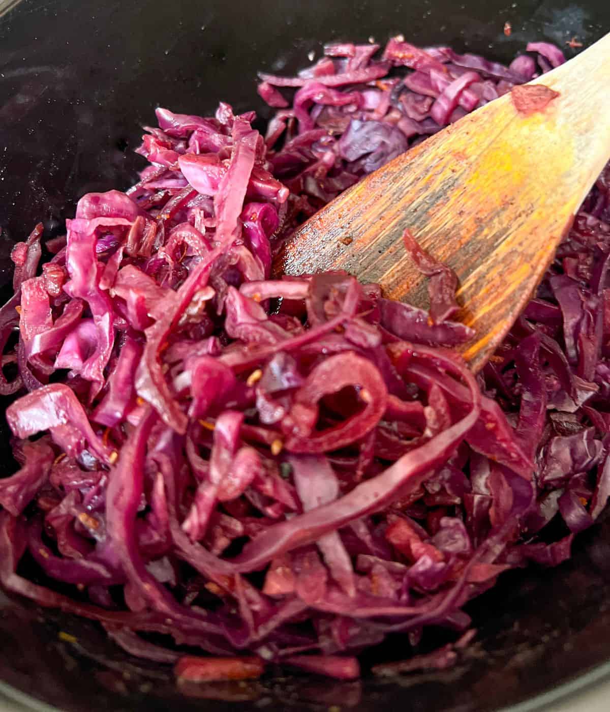 Sliced cooked red cabbage being stirred with a wooden spoon.