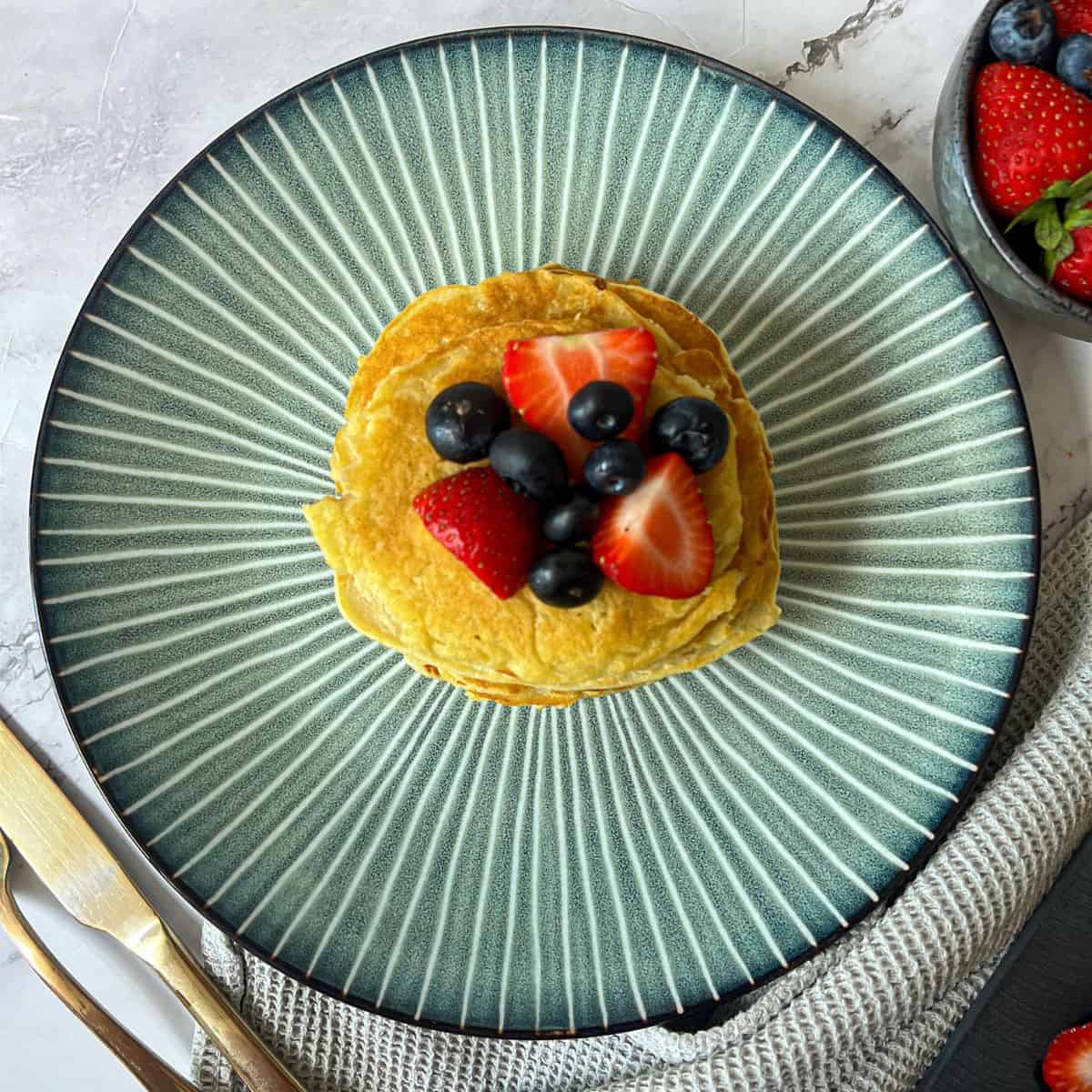 A pile of pancakes on a striped plate, topped with strawberries and blueberries.