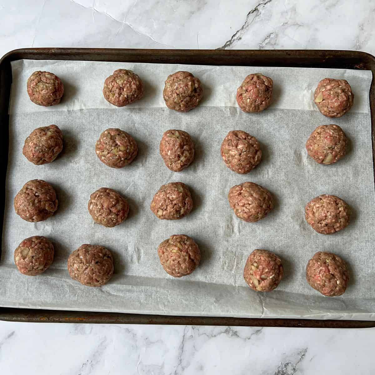 20 raw meatballs on a baking tray.