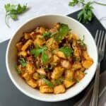 A bowl of roasted swede cubes garnished with fresh parsley. There is a fork and some fresh parsley in the background.